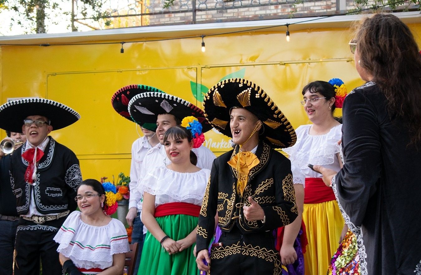 A woman is standing in front of a group of people dressed in traditional mexican clothing.