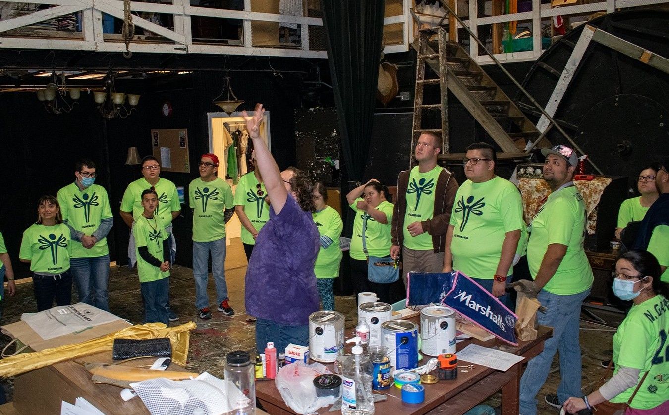 A group of people wearing green shirts are standing around a table.