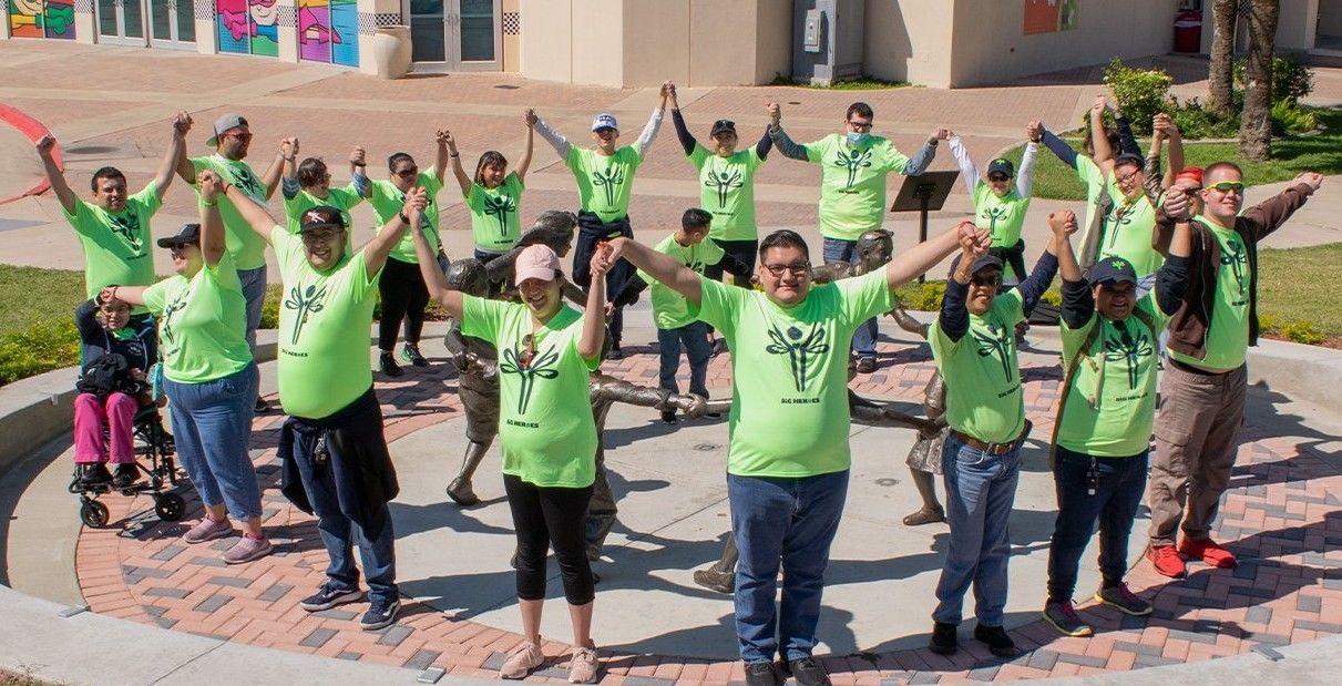 A group of people wearing green shirts are standing in a circle with their arms in the air.