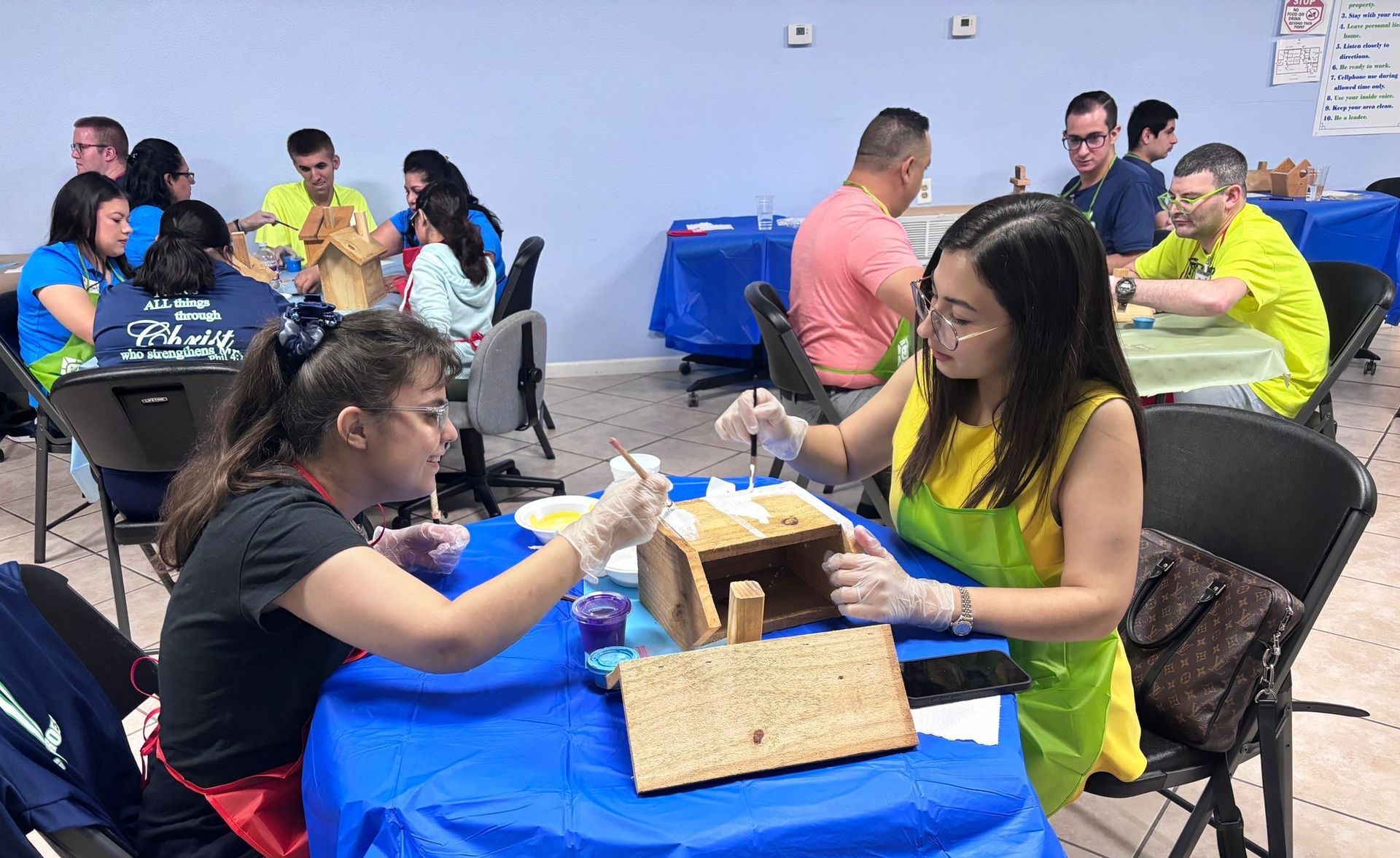 A group of people are sitting at tables making gingerbread houses.