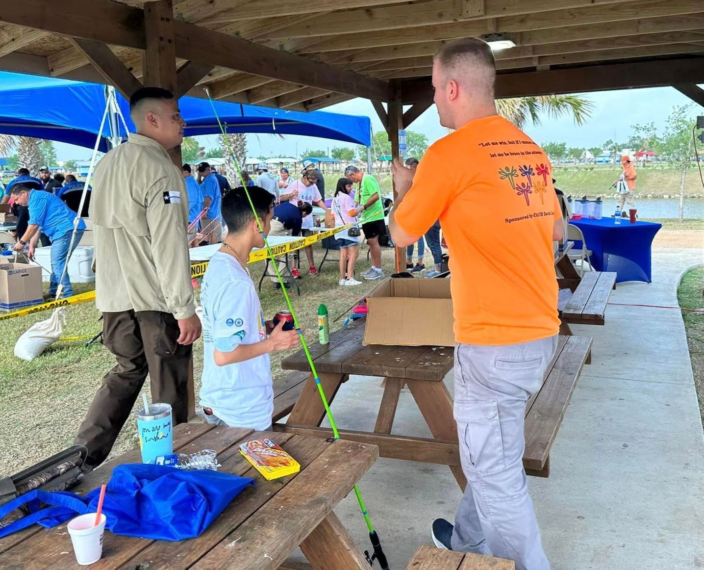 A man in an orange shirt is standing next to a boy holding a fishing rod.