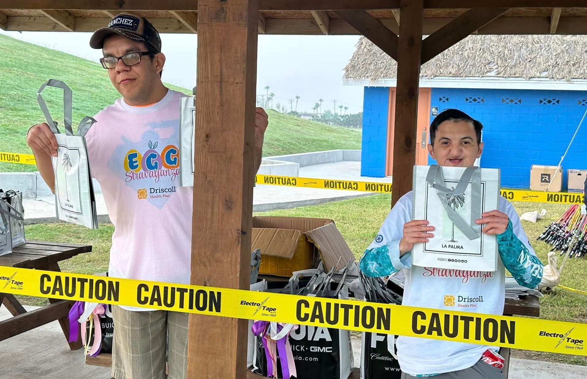A man and a boy are standing under a pavilion holding medals behind a caution tape.