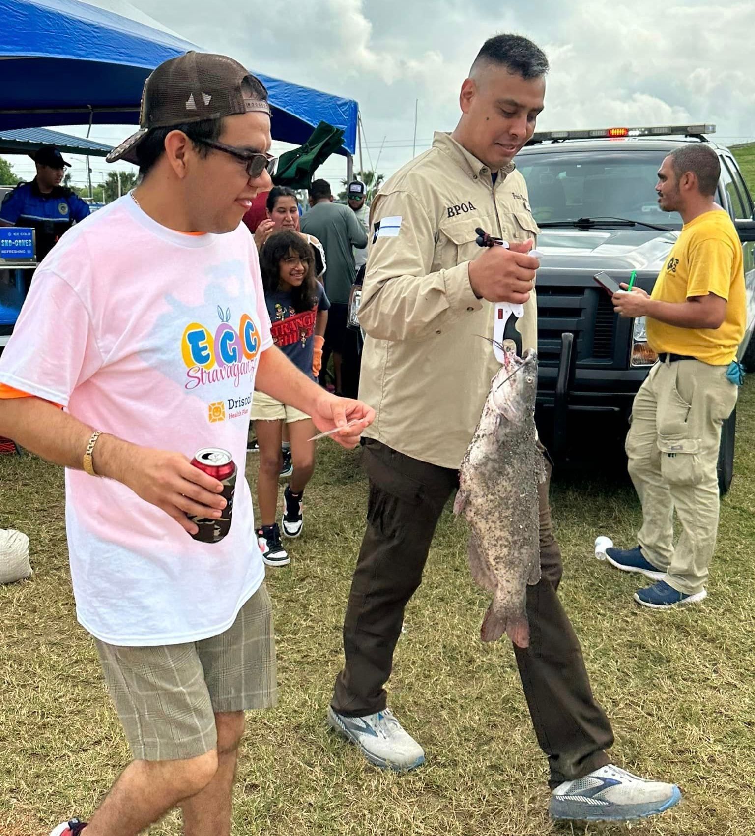 A group of men are standing in a field holding a fish.