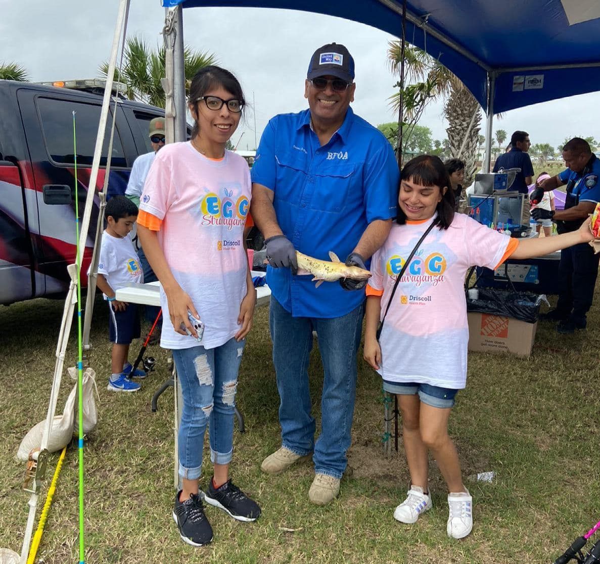 A man and two girls are standing under a tent holding a fish.