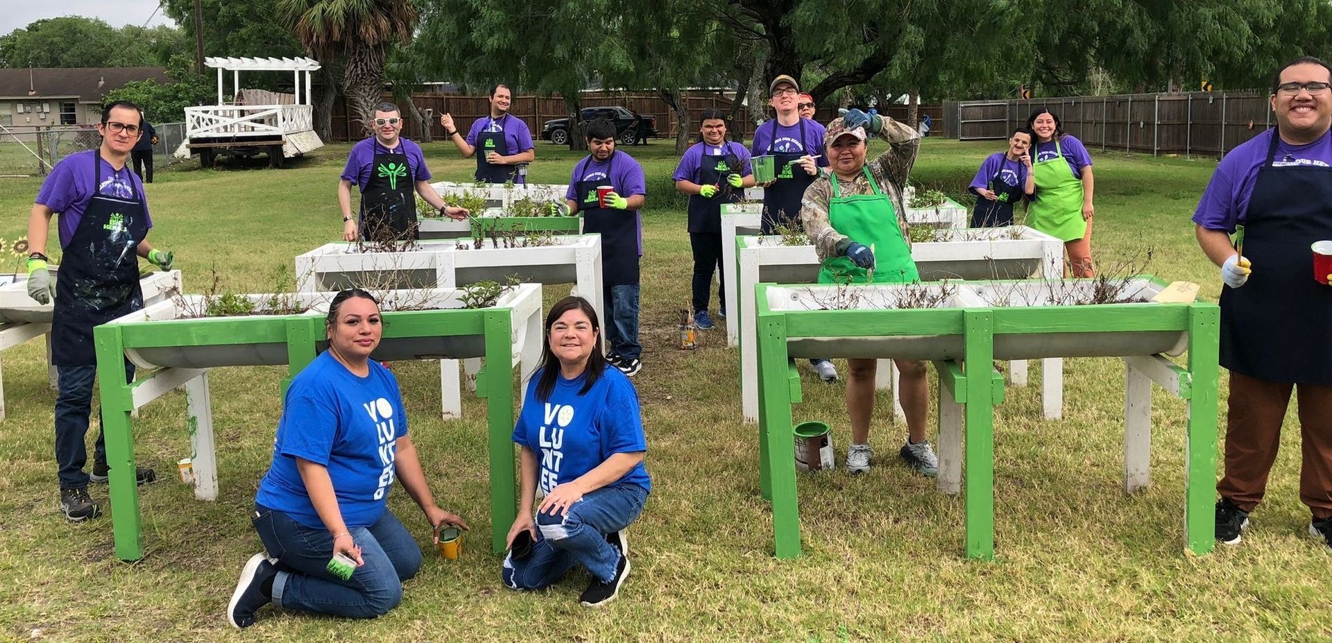 A group of people are kneeling in front of tables in a field.