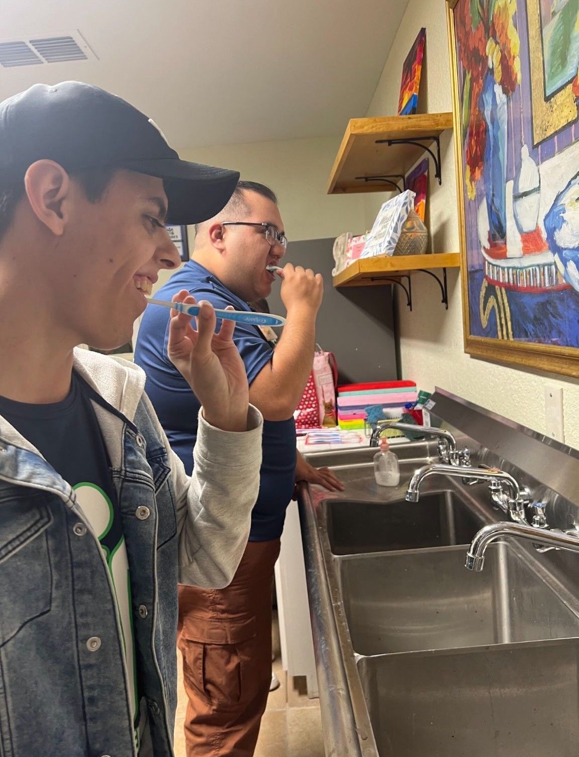 Two men are brushing their teeth in a kitchen sink