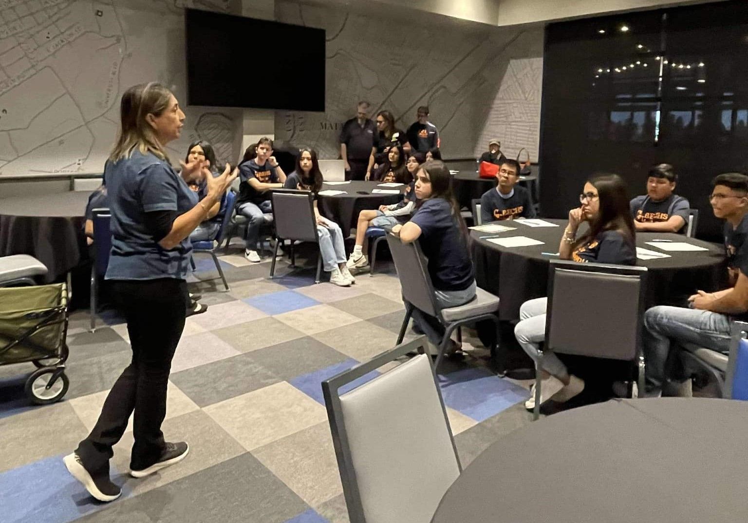 A woman is standing in front of a group of people sitting at tables.