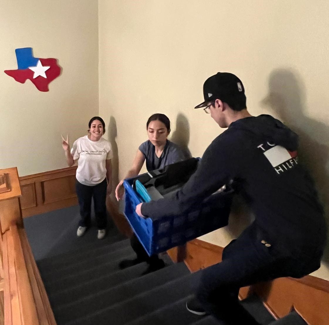 A man is carrying a blue crate with a texas flag on the wall behind him