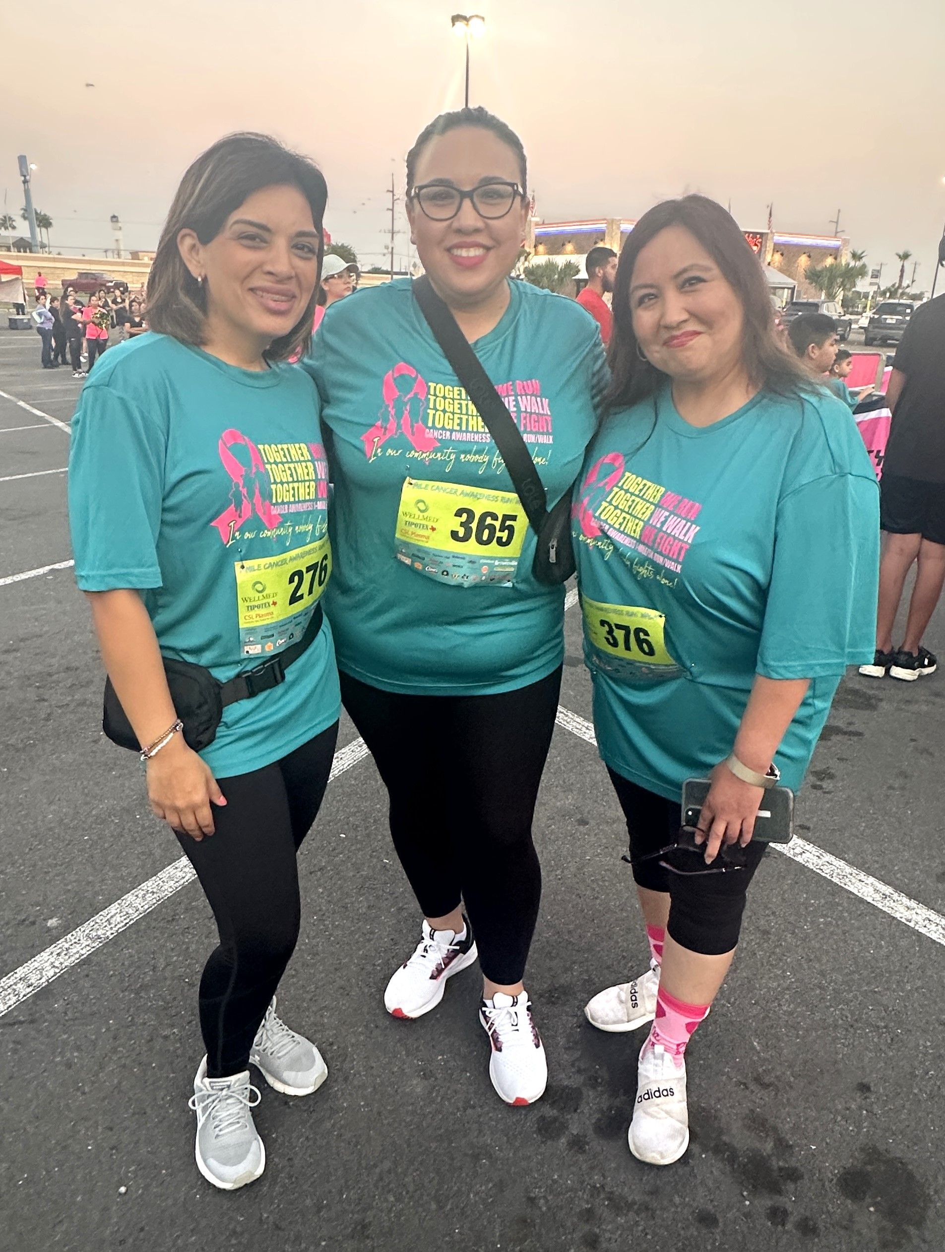 Three women are posing for a picture in a parking lot.