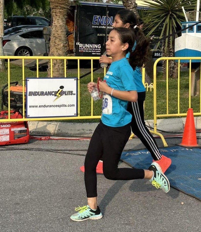 Two girls are running in front of a sign that says endurance plus