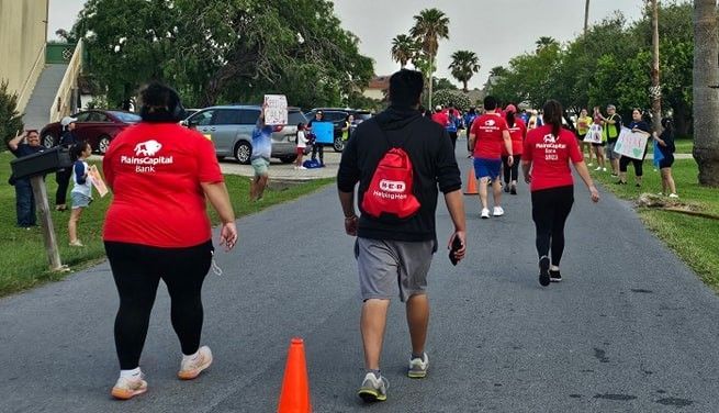 A group of people walking down a street wearing red shirts with the letter b on them