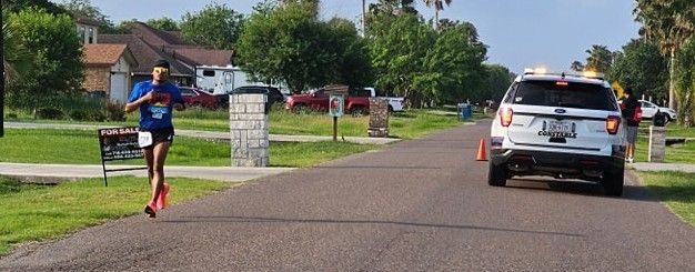 A person is running down a street next to a police car.