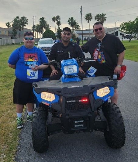 Three men are posing for a picture while one of them is riding an atv