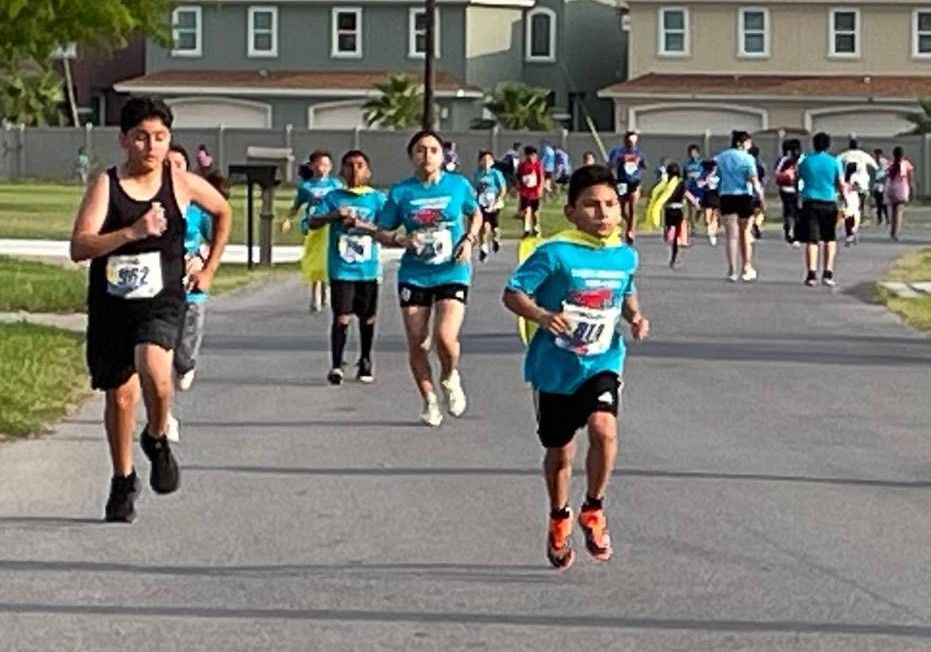 A group of children are running down a street with numbers on their shirts