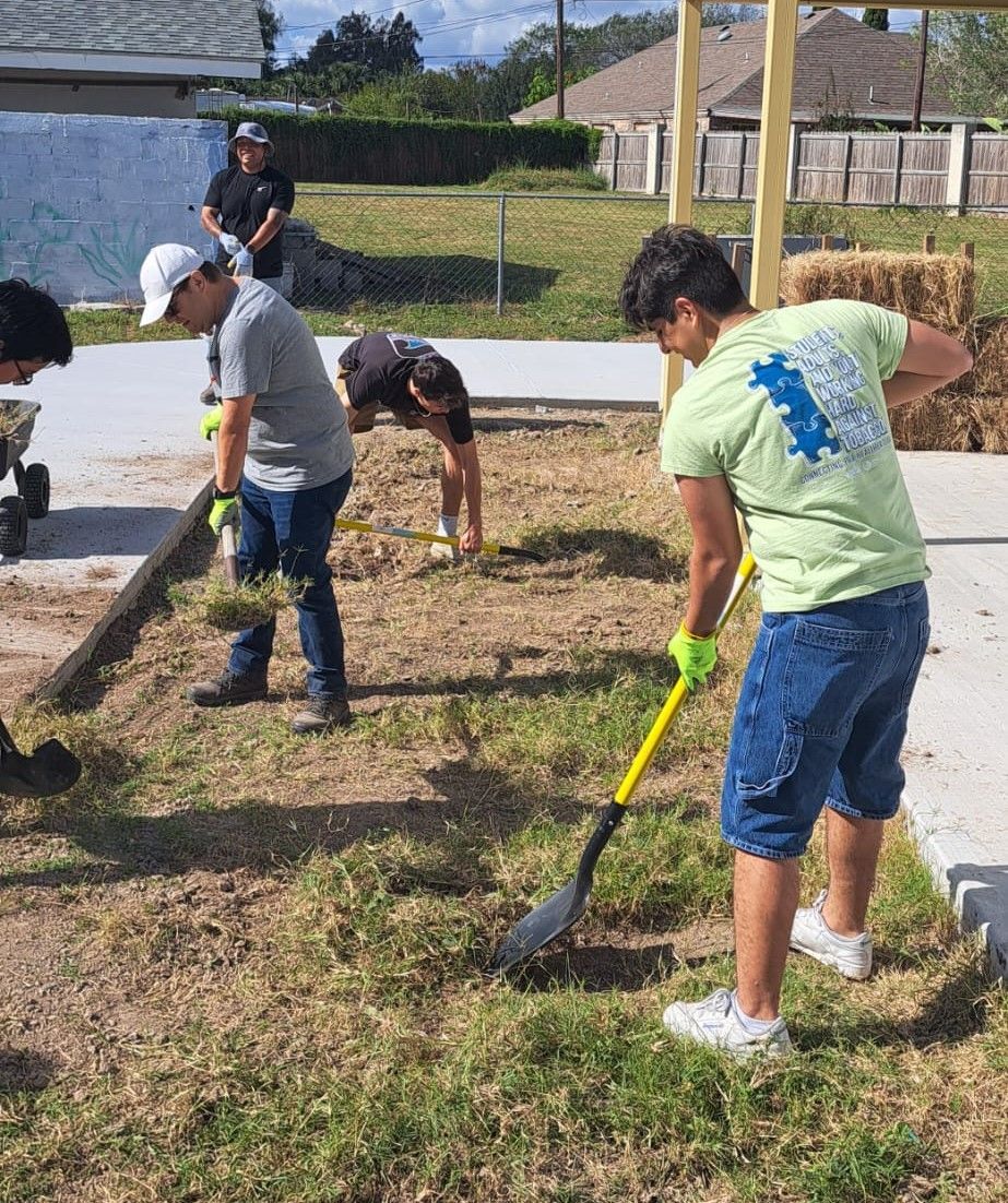 A group of people are working in a yard with shovels and rakes.