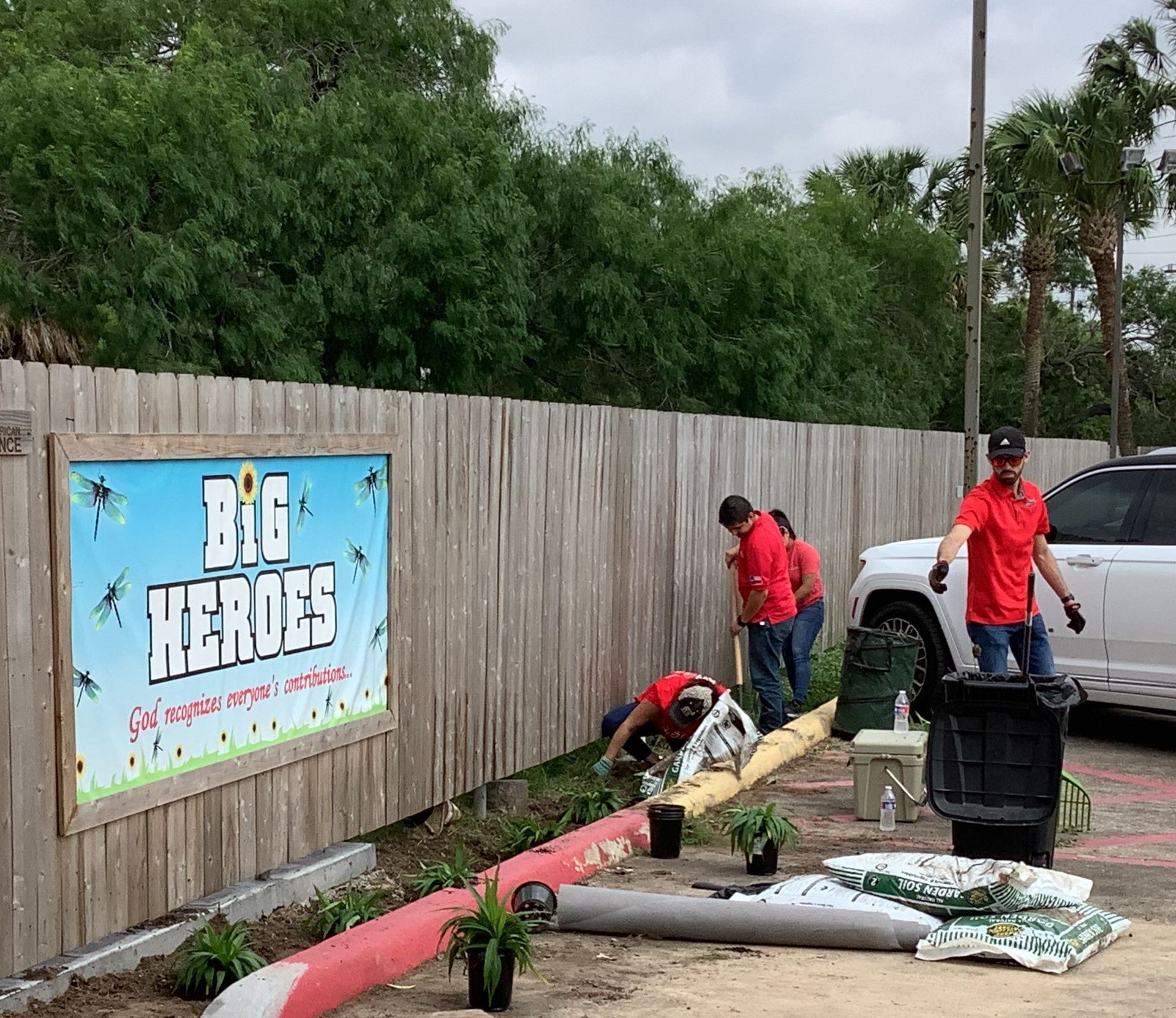 A group of people are working in a garden in front of a sign that says big heroes.