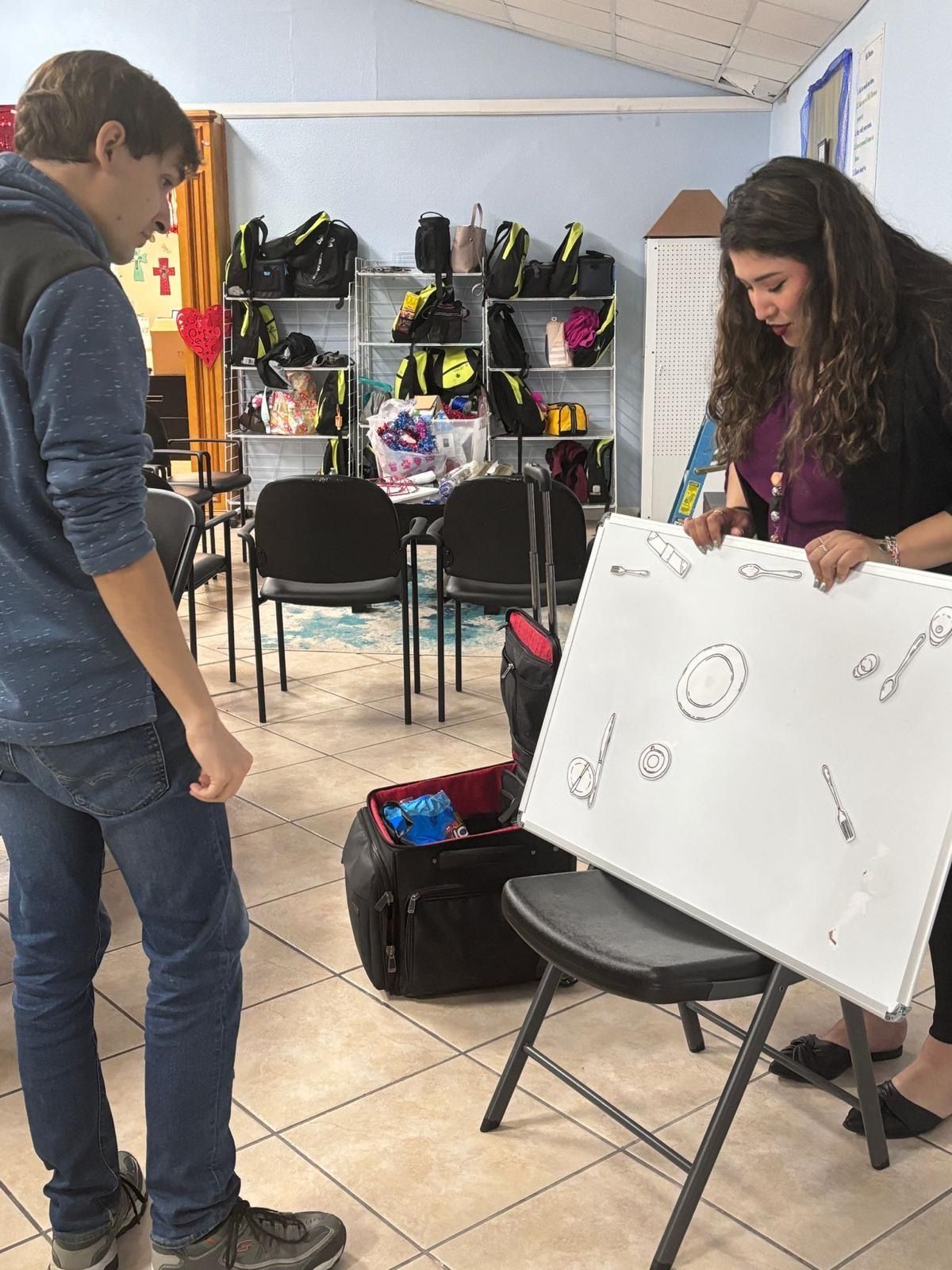 A man and a woman are standing in a room holding a white board.