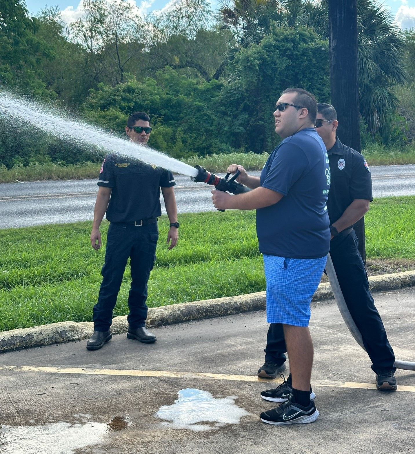 A man is spraying water from a fire hose in a parking lot.