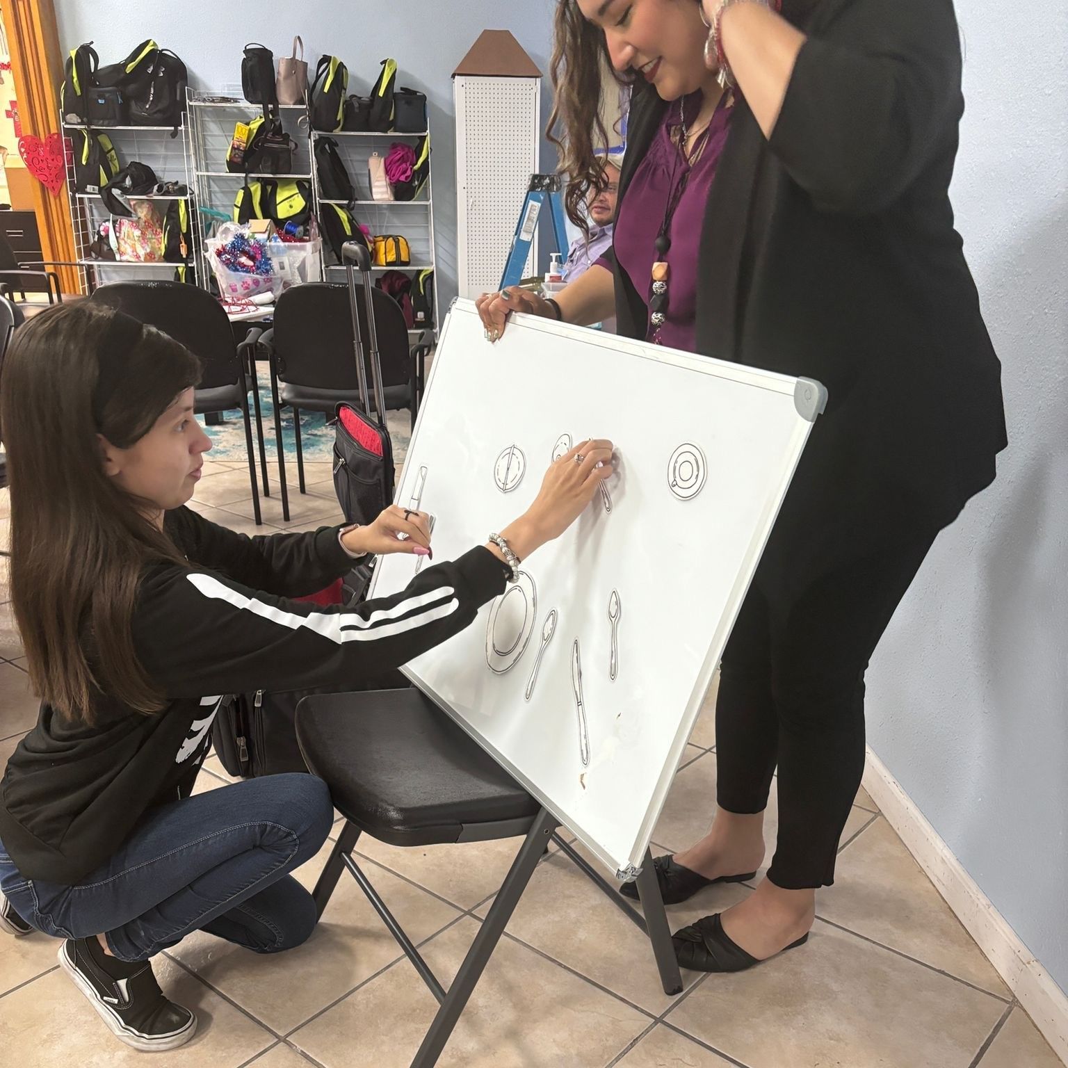 Two women are drawing on a white board in a room