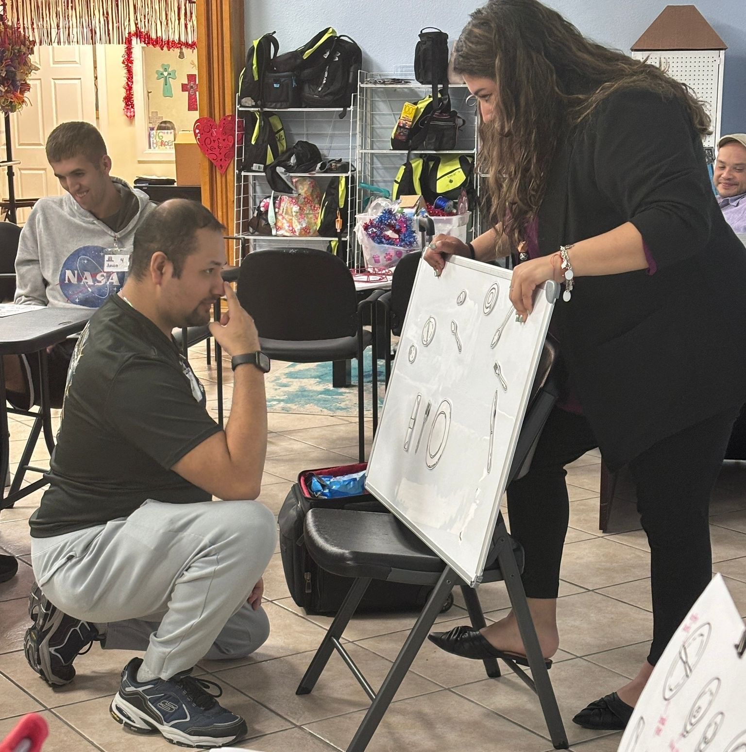 A man wearing a nasa shirt is kneeling down in front of a white board