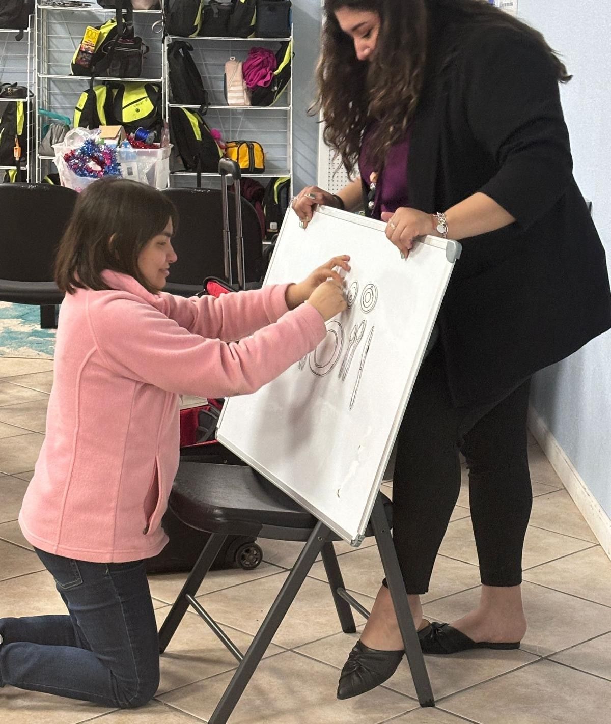 A woman is helping a little girl draw on a white board