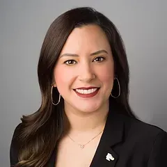 A woman wearing a black jacket and earrings is smiling for the camera.
