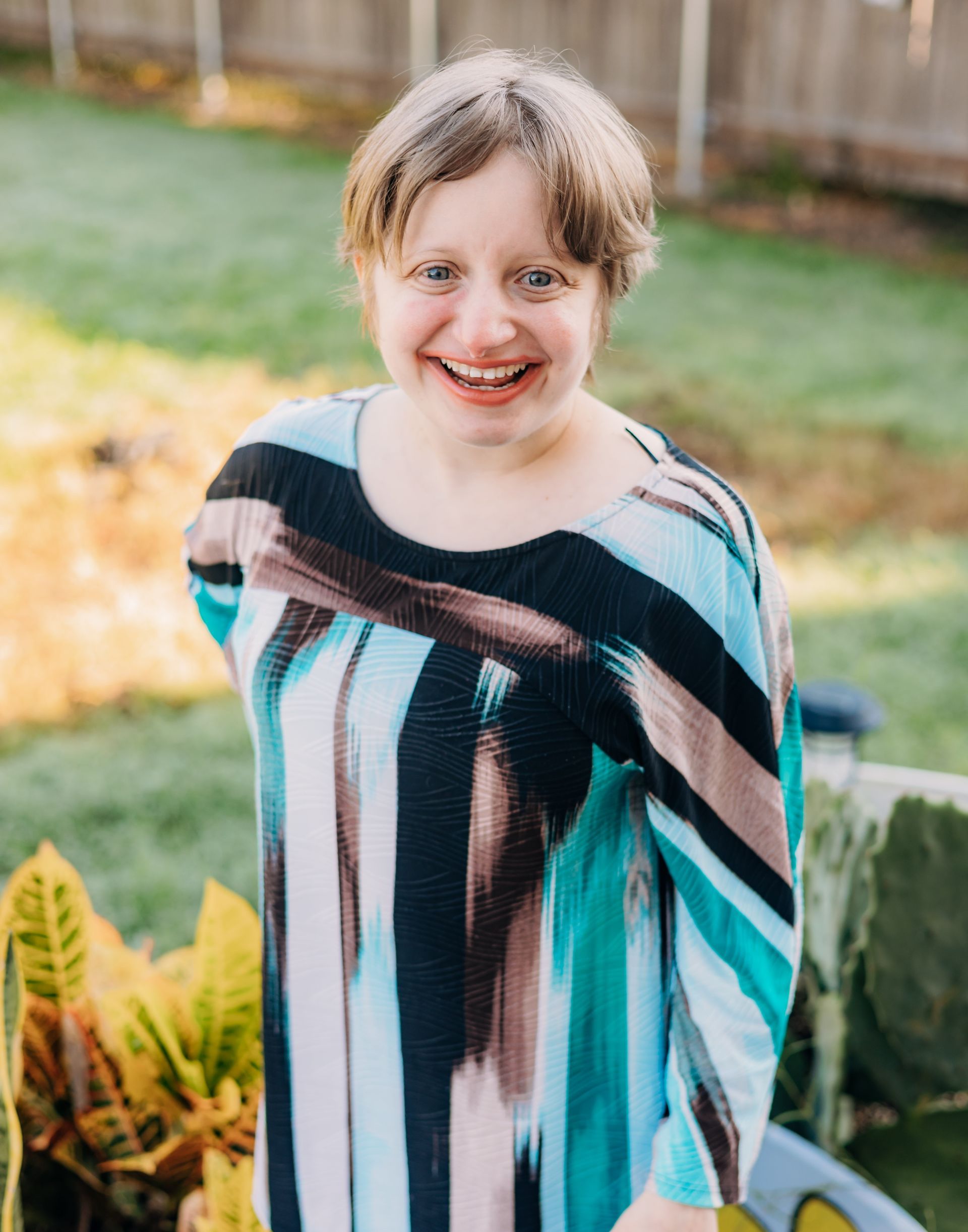 A woman in a striped dress is standing in the grass and smiling.