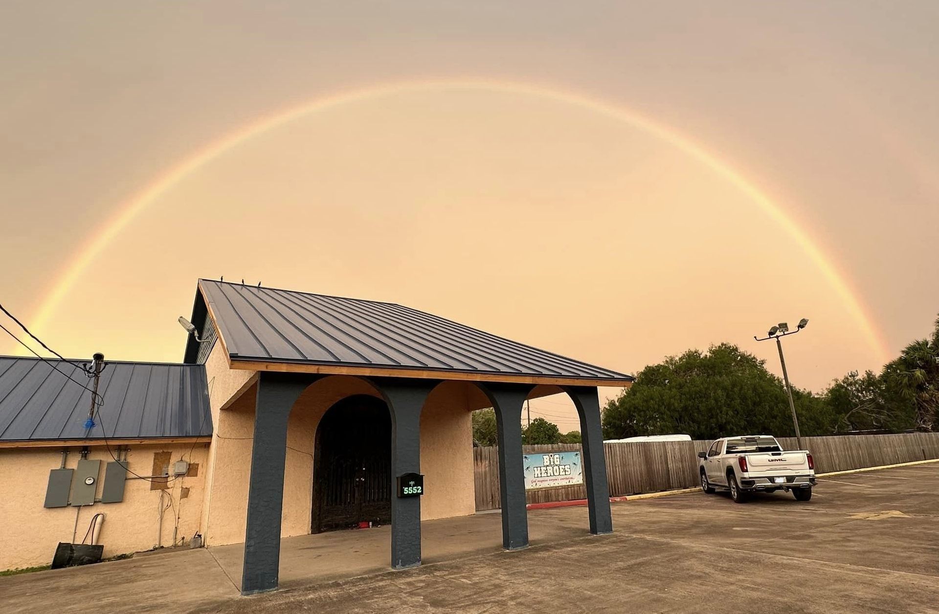 A car is parked in front of a building with a rainbow in the sky