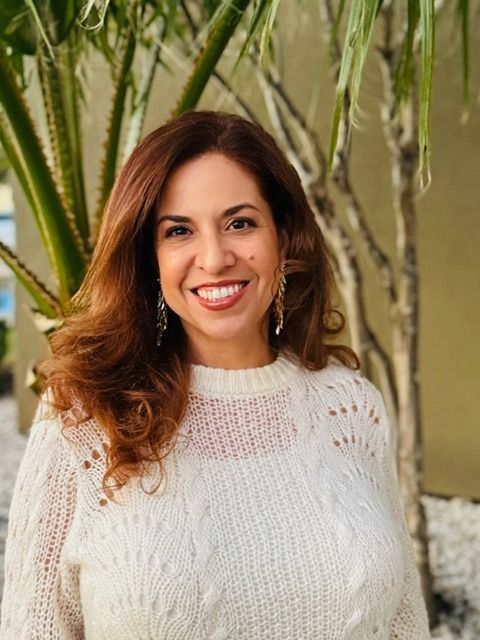 A woman in a white sweater is smiling in front of a palm tree.