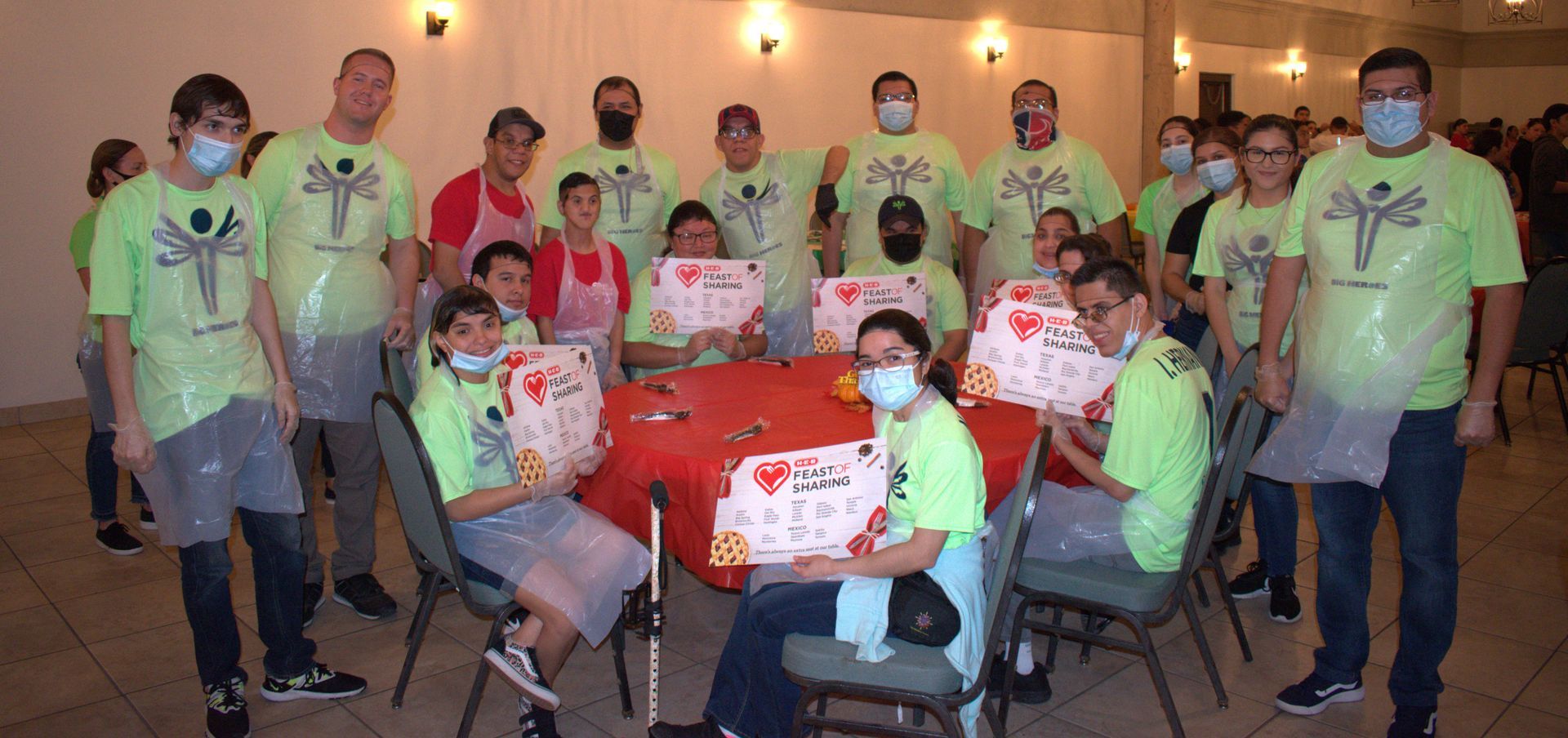 A group of people wearing masks are standing around a table holding signs.