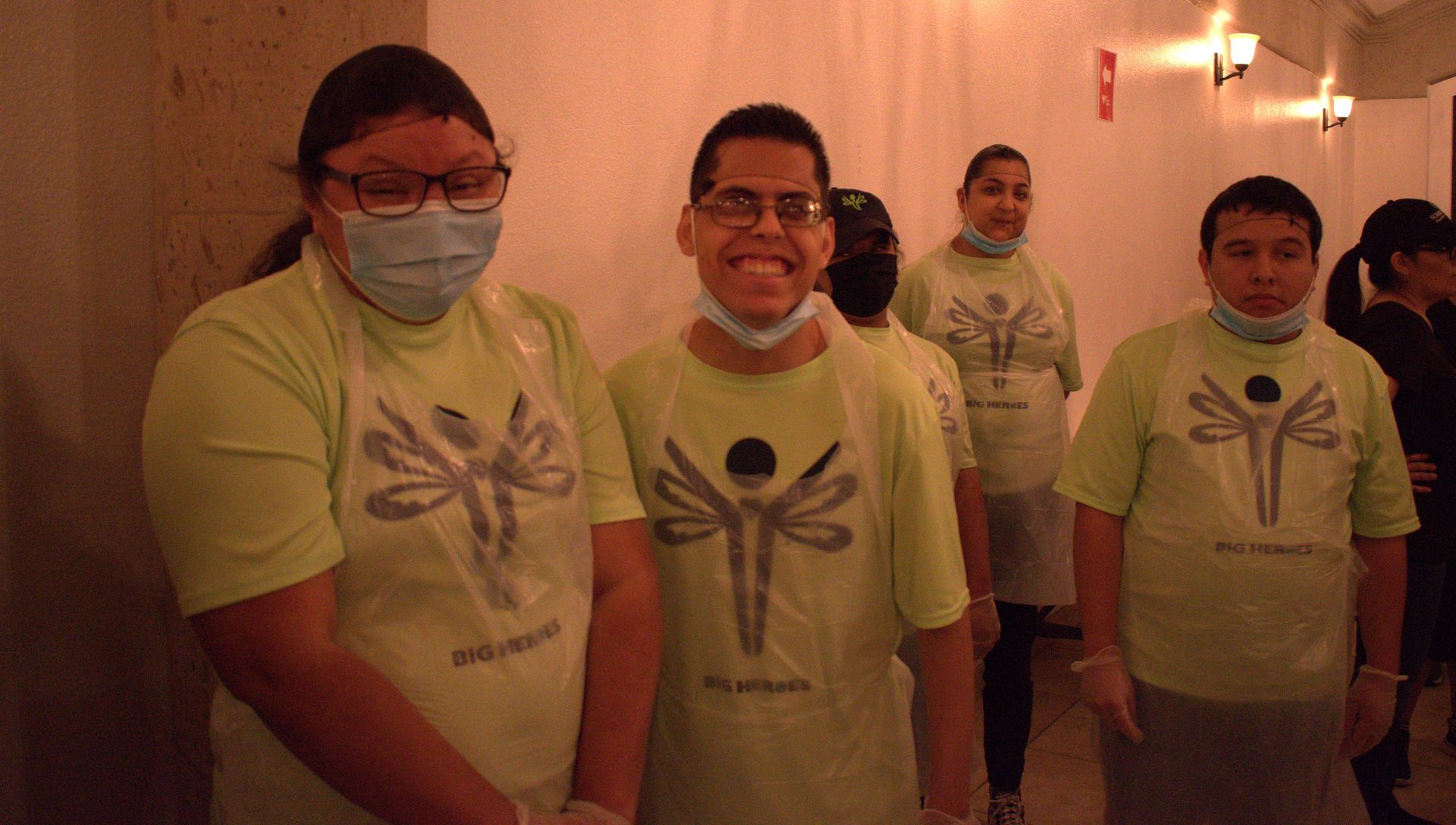 A group of people wearing masks and green shirts are standing next to each other.