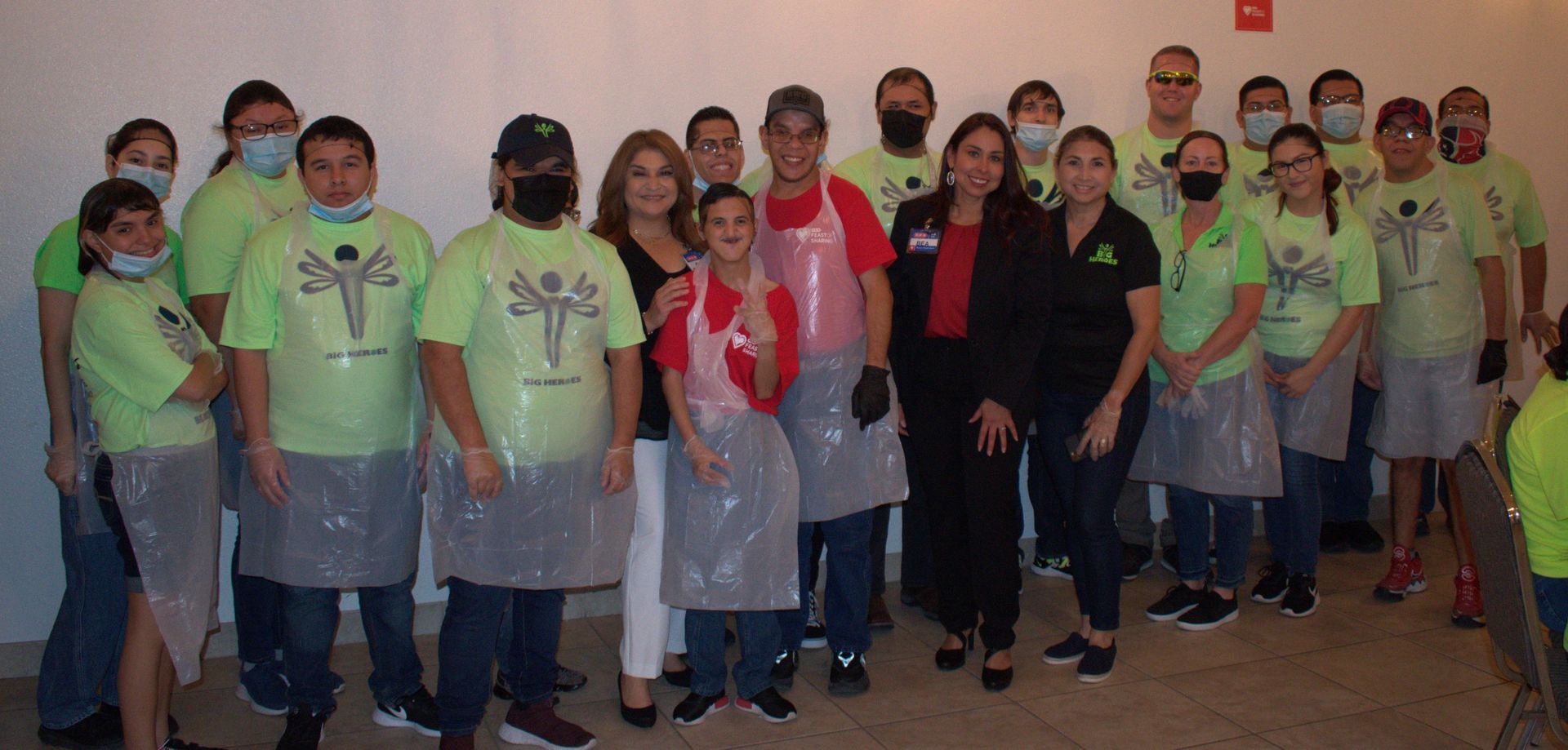 A group of people wearing green shirts and plastic aprons are posing for a picture.