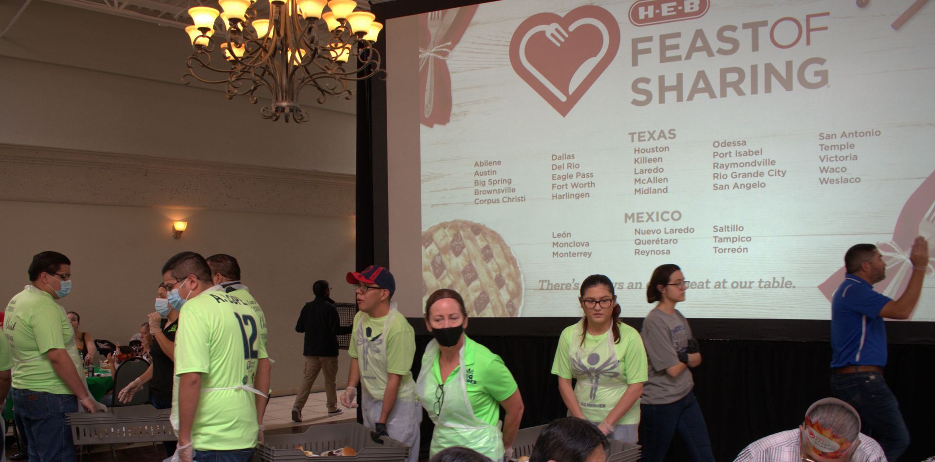 A group of people are standing in front of a large screen that says feast of sharing.