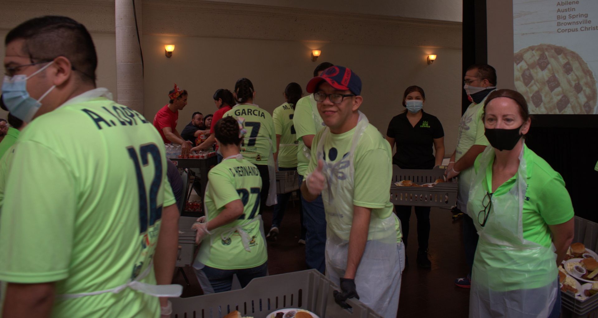 A group of people wearing masks and green shirts are standing in a room.