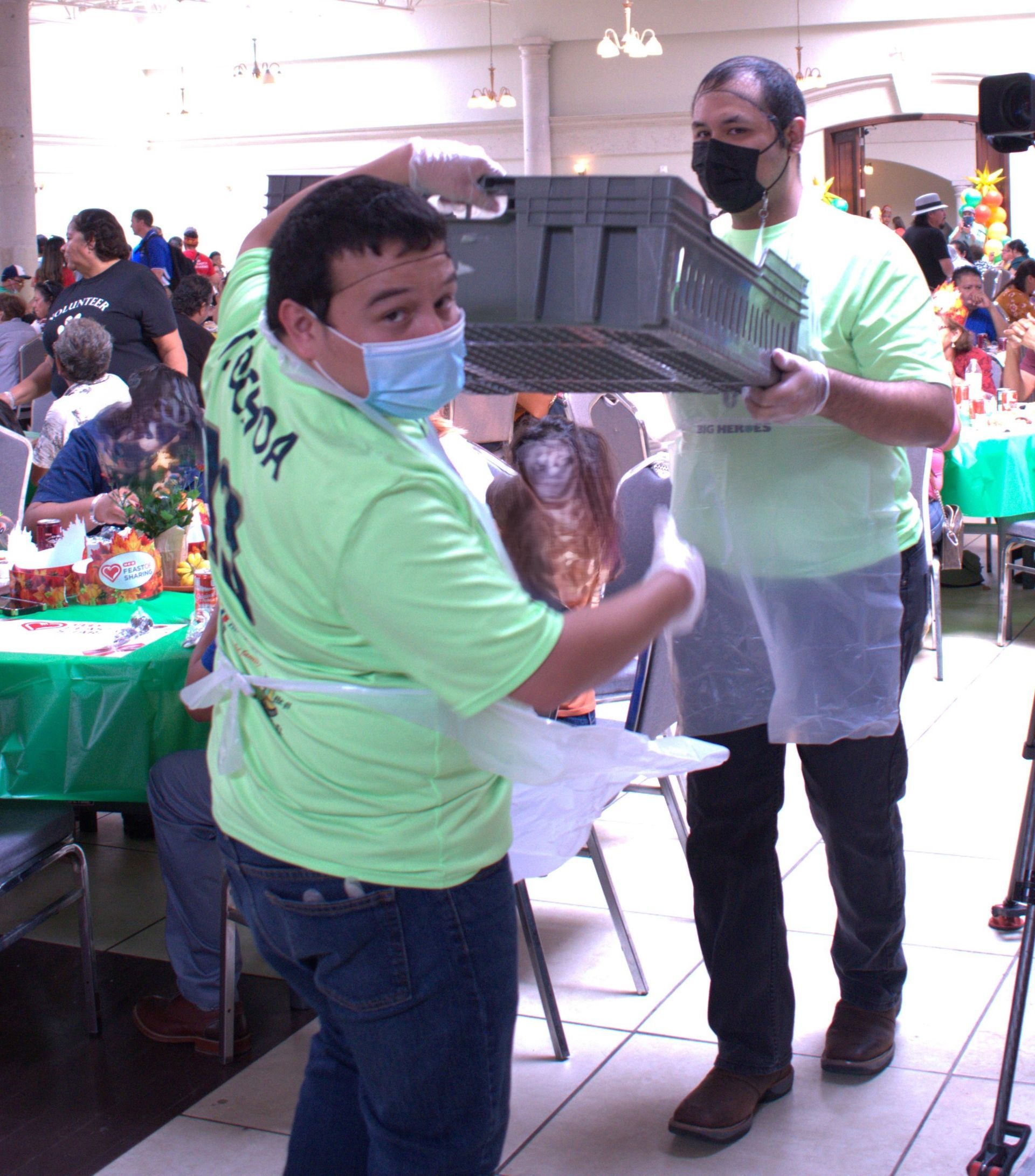 A man wearing a mask holds a crate while another man stands behind him