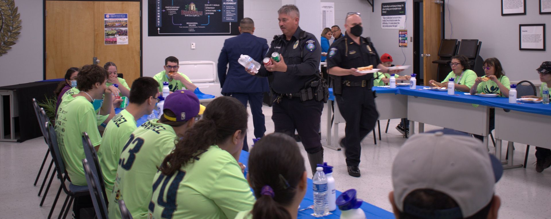 A group of people are sitting at tables in a room with police officers.
