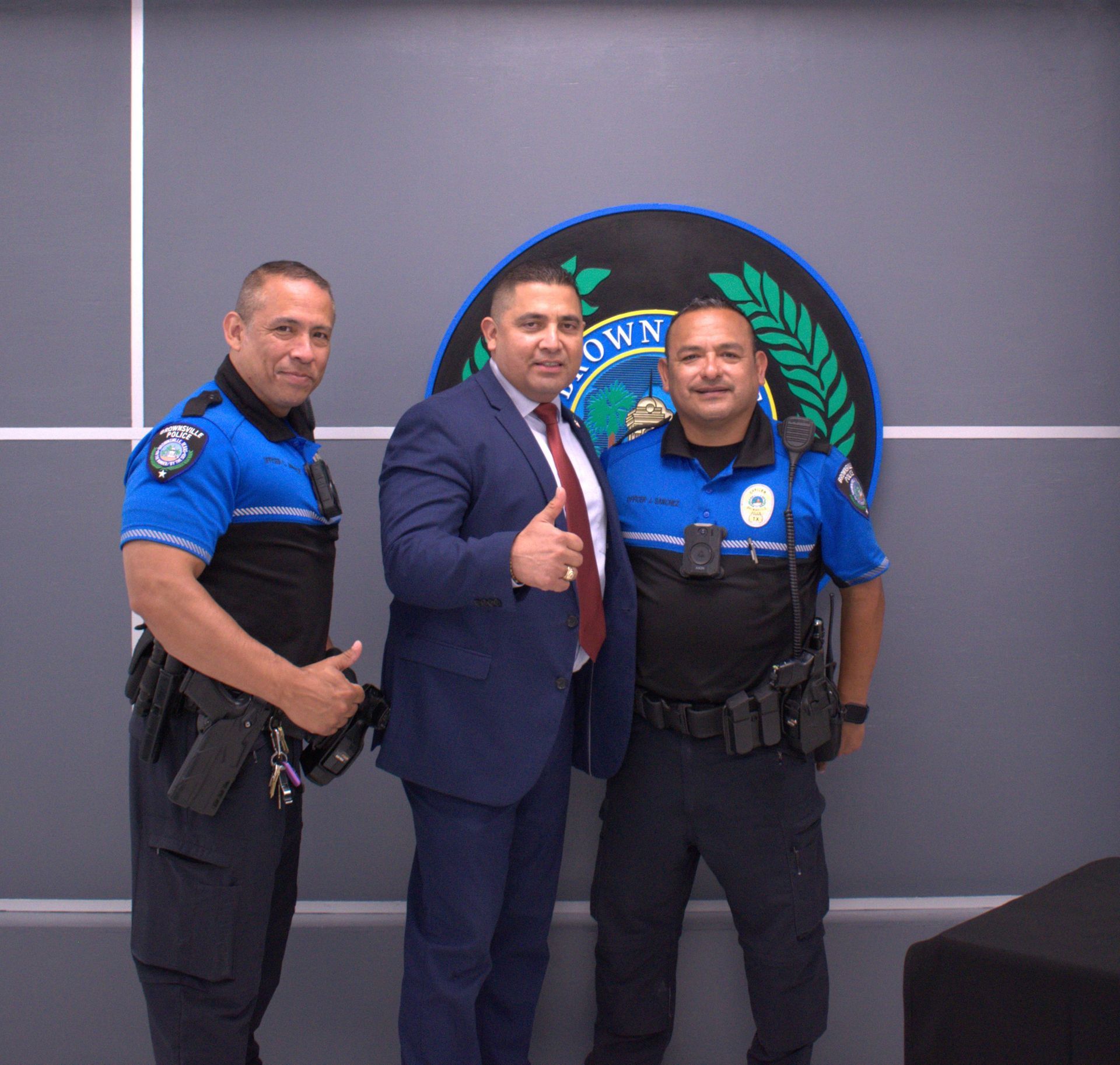 Three police officers are posing for a picture in front of a sign that says own