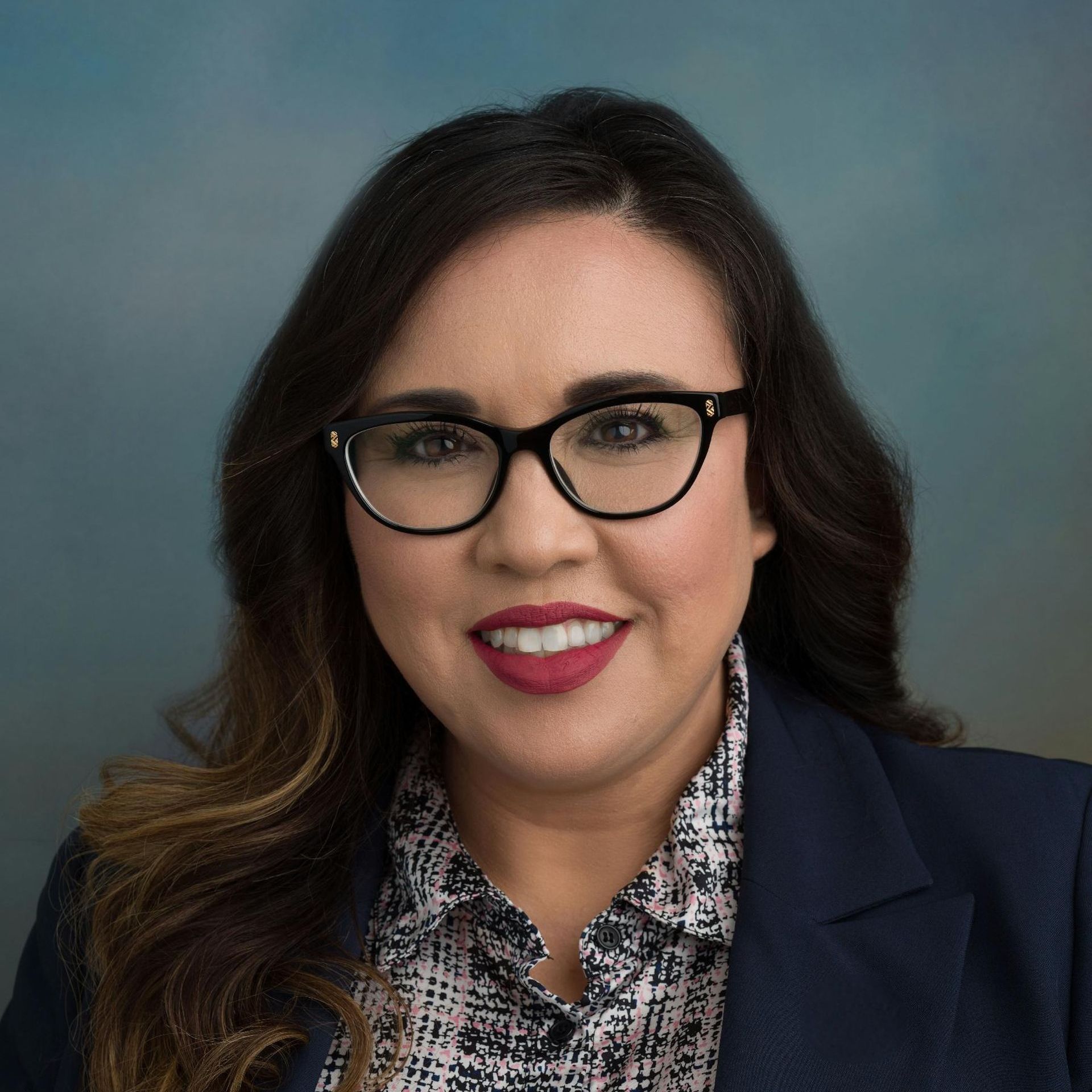 A woman wearing glasses and a jacket is smiling for the camera.