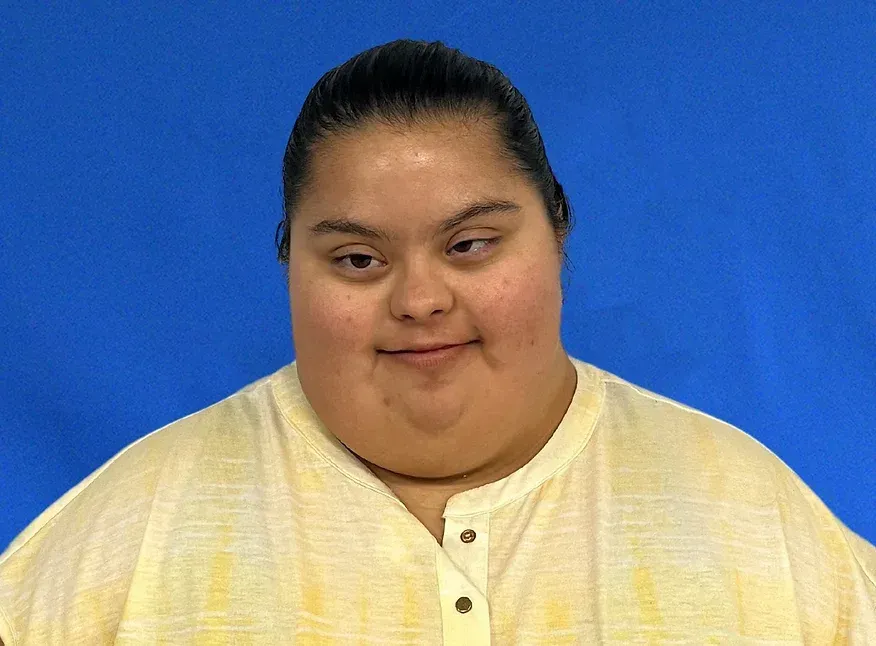 A woman with down syndrome is smiling in front of a blue background.