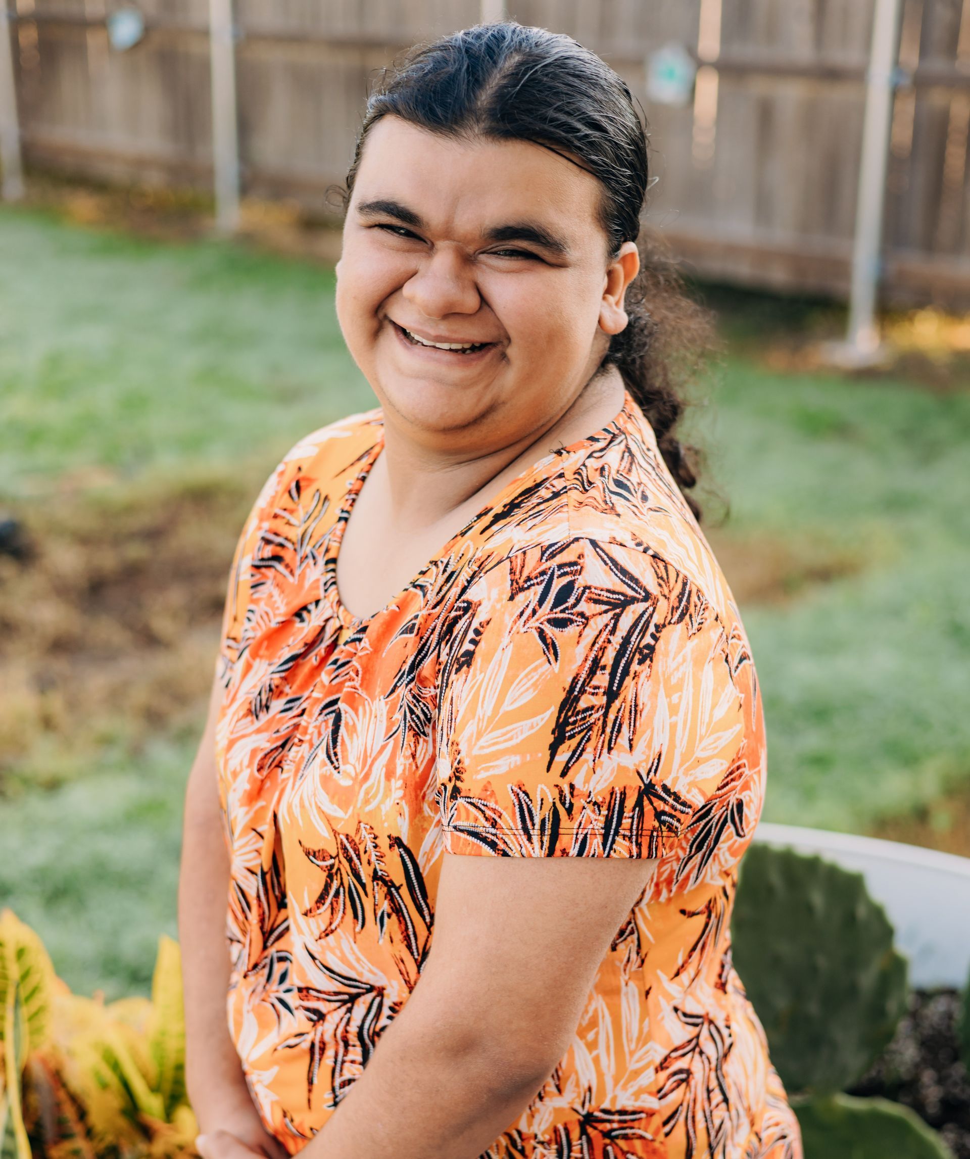 A woman in an orange shirt is standing in front of a cactus and smiling.