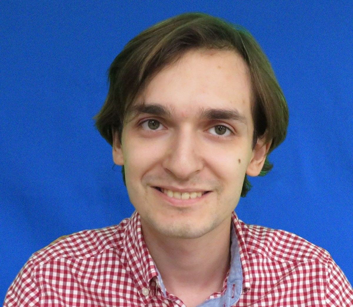 A man in a plaid shirt is smiling in front of a blue background