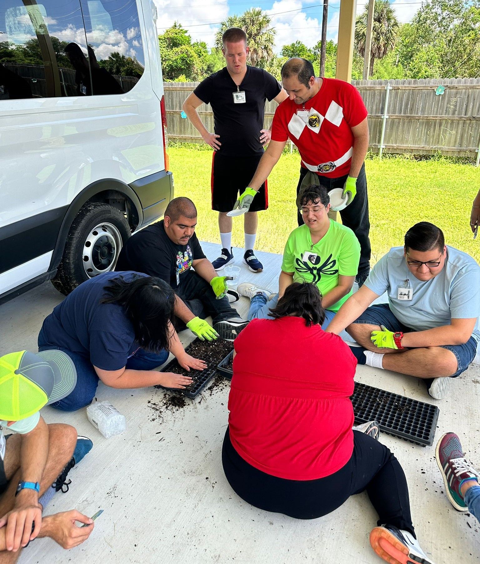 A group of people are sitting on the ground in front of a van.