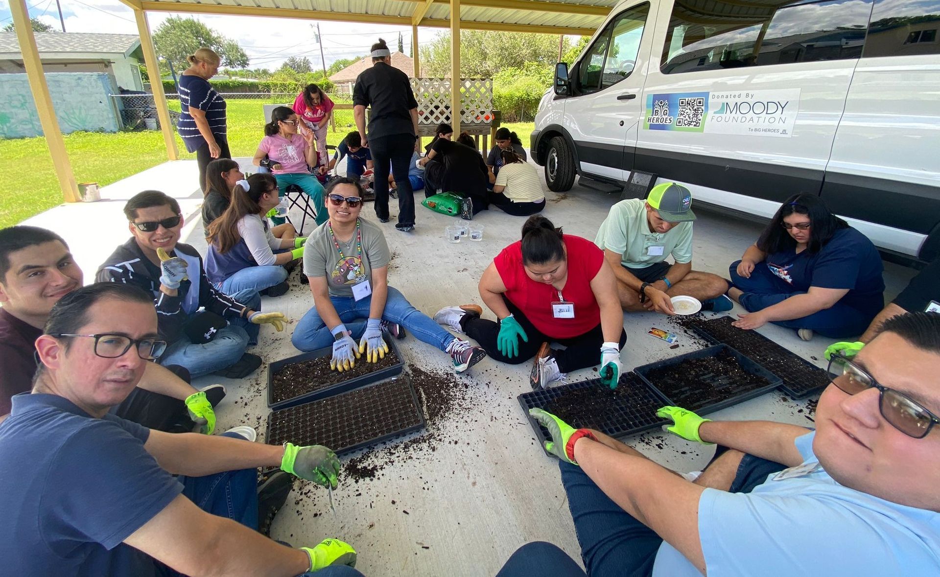 A group of people are sitting on the ground in front of a van.