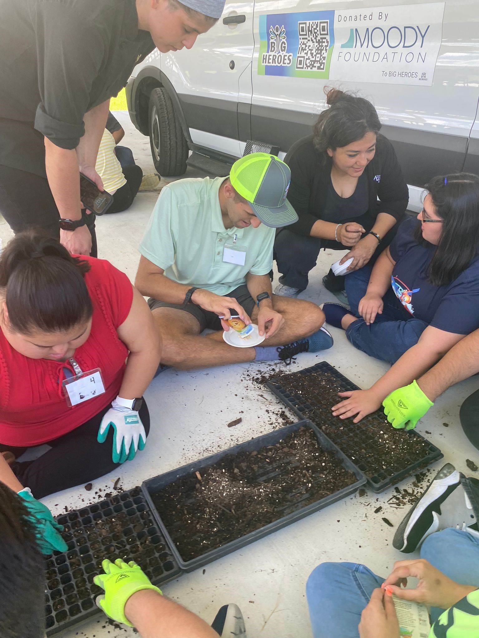 A group of people are sitting on the ground planting plants.