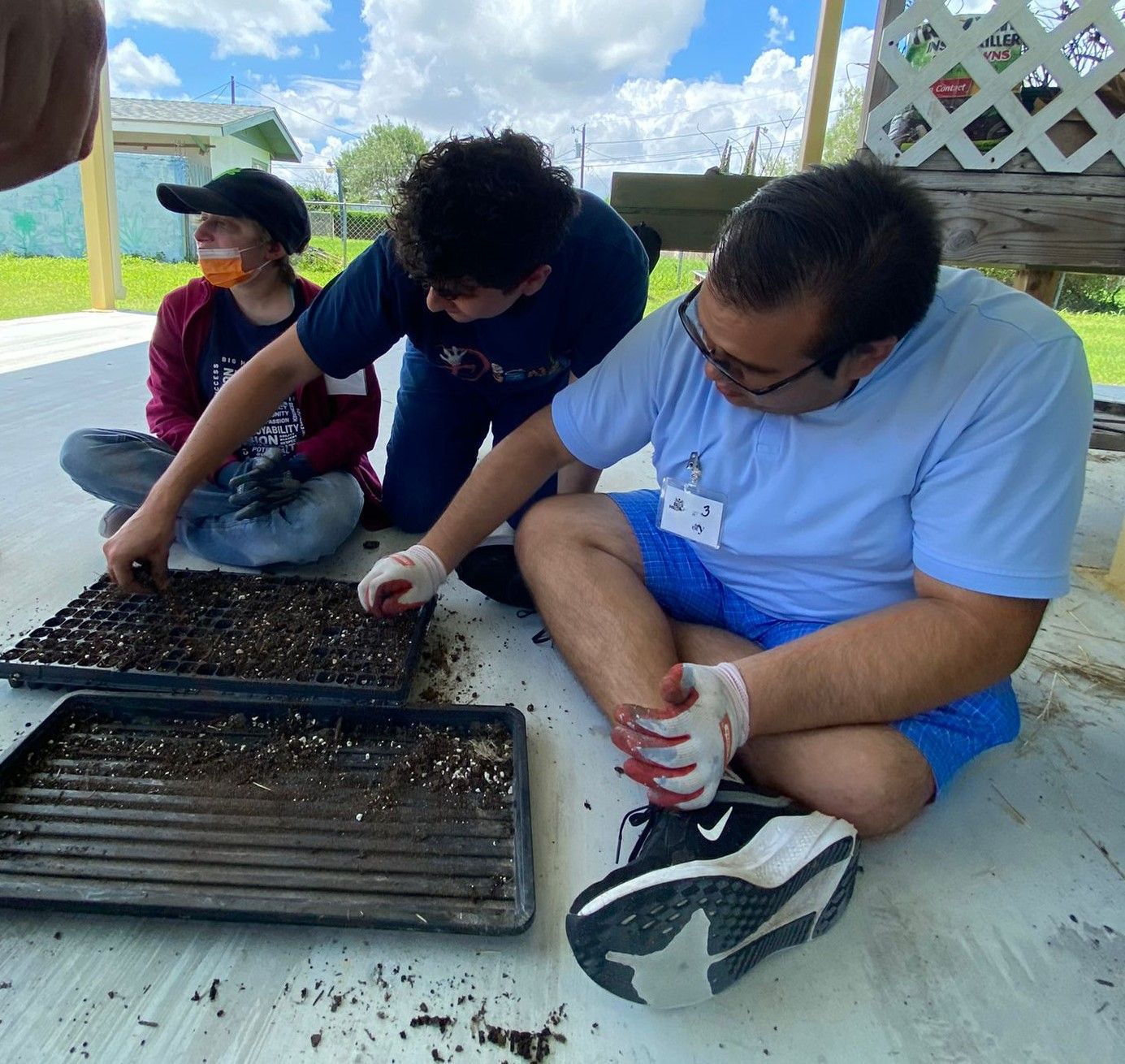 A group of people are sitting on the ground with trays of dirt