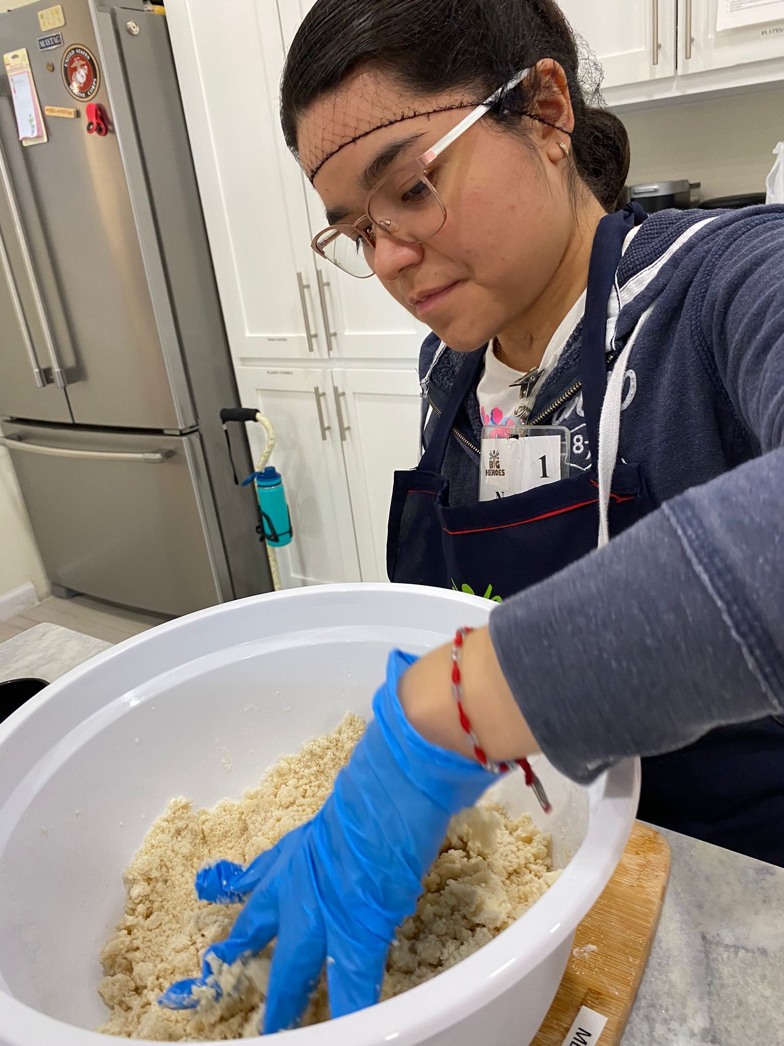 A woman wearing blue gloves is mixing a bowl of food.