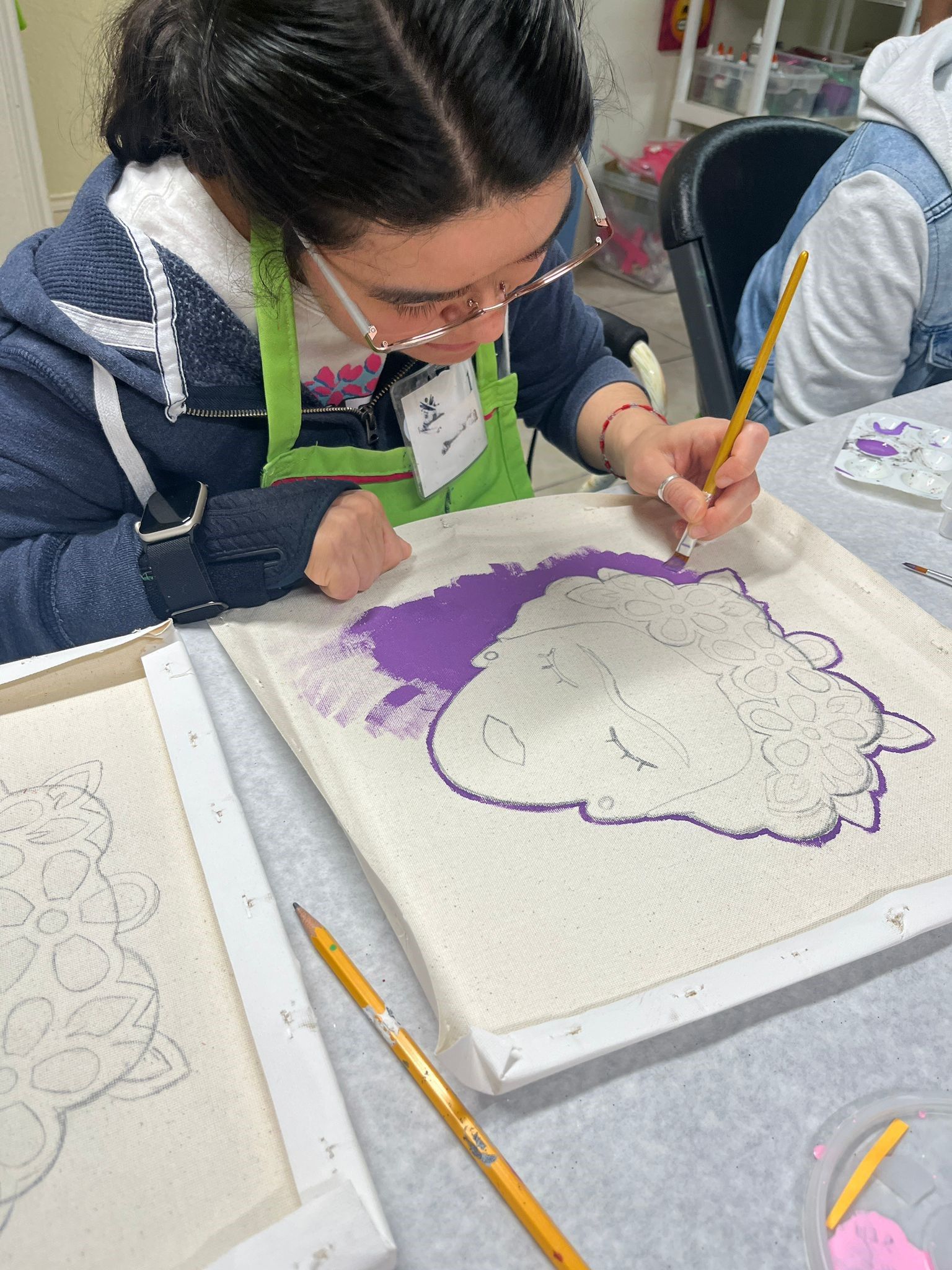 A woman is sitting at a table painting on a canvas.