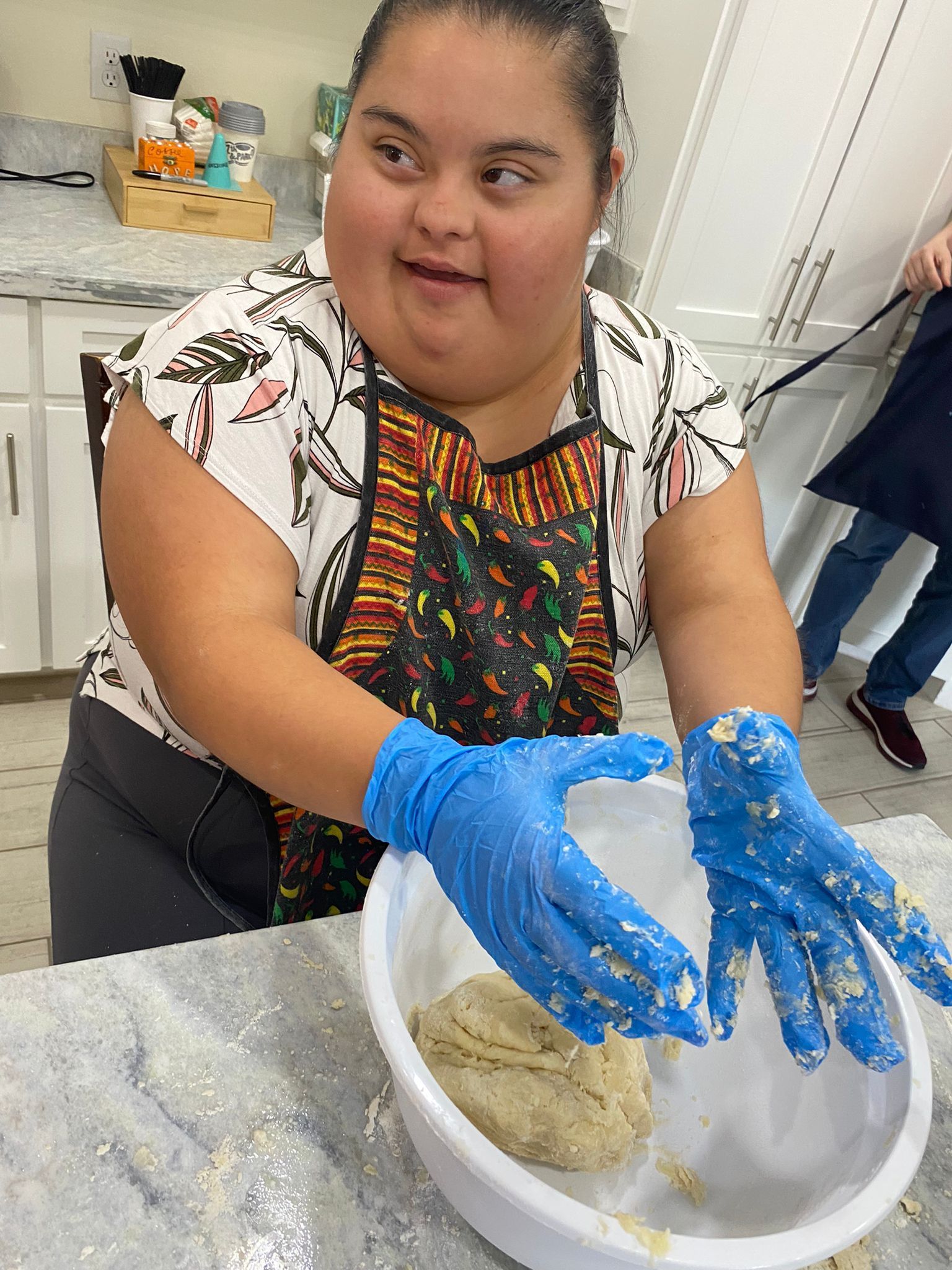 A woman wearing blue gloves is mixing dough in a bowl.