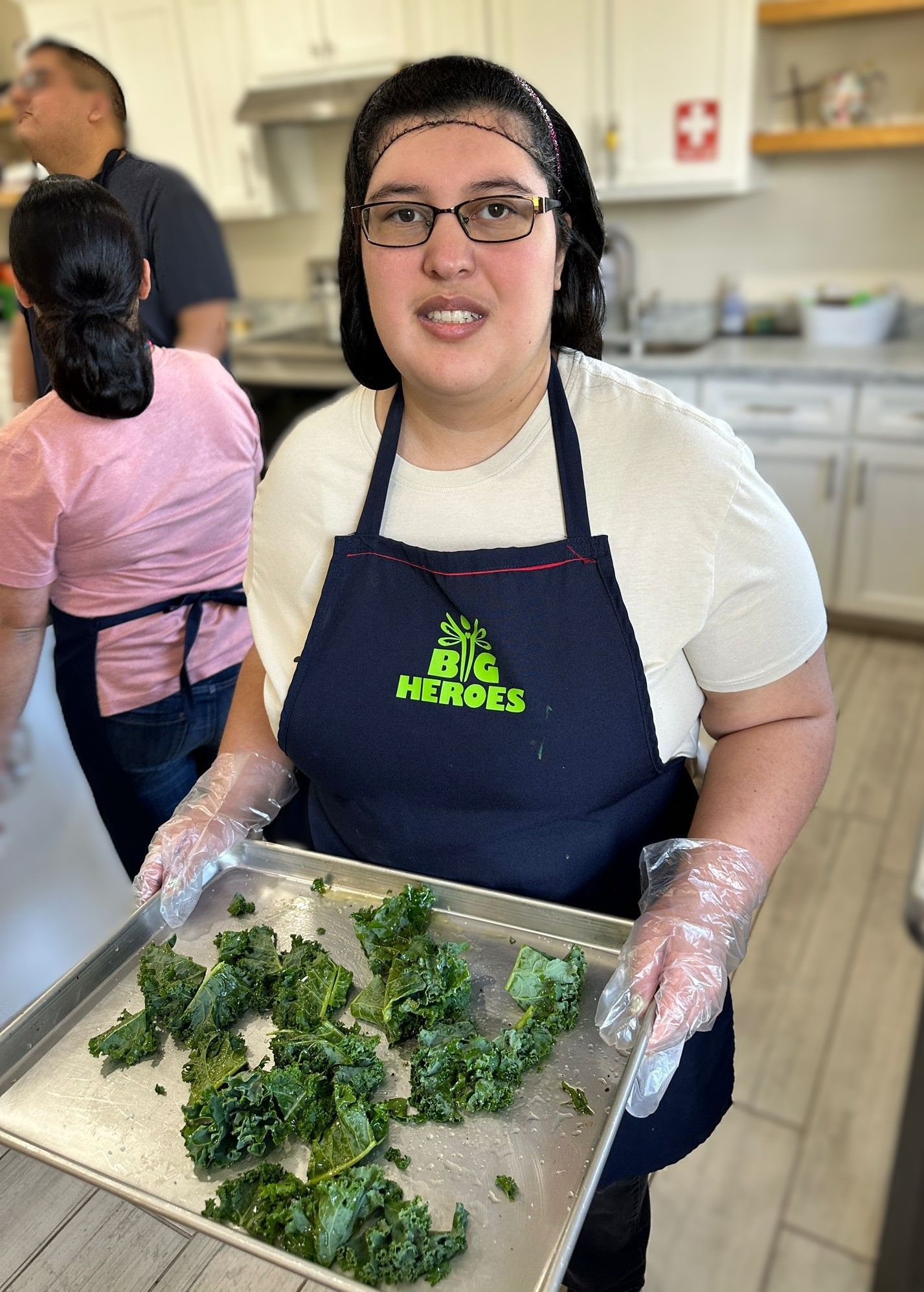 A woman in an apron is holding a tray of kale.