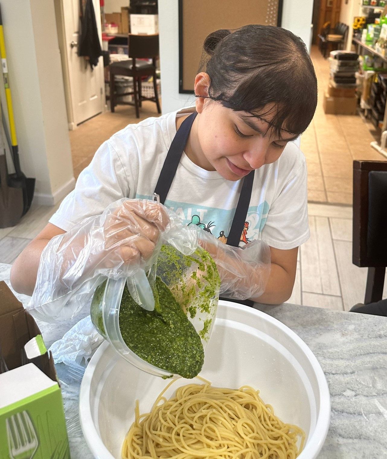 A woman is pouring pesto into a bowl of spaghetti.